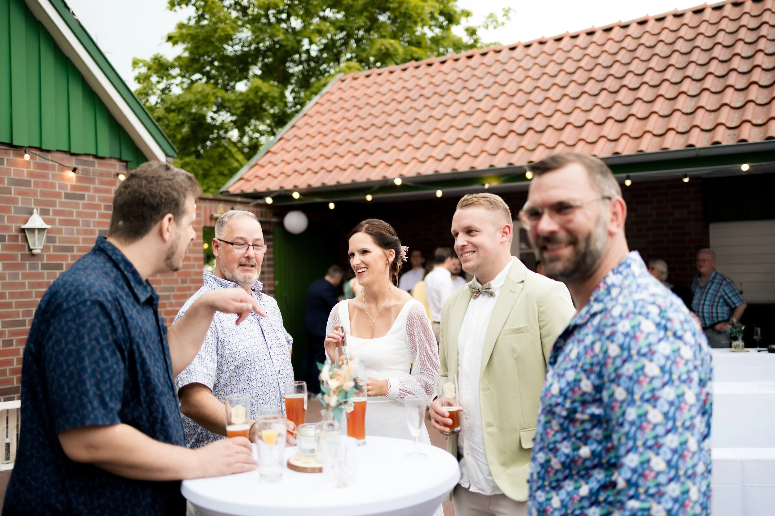 Menschen beim Feiern im Garten mit Getränken, vermutlich bei einer Hochzeit.