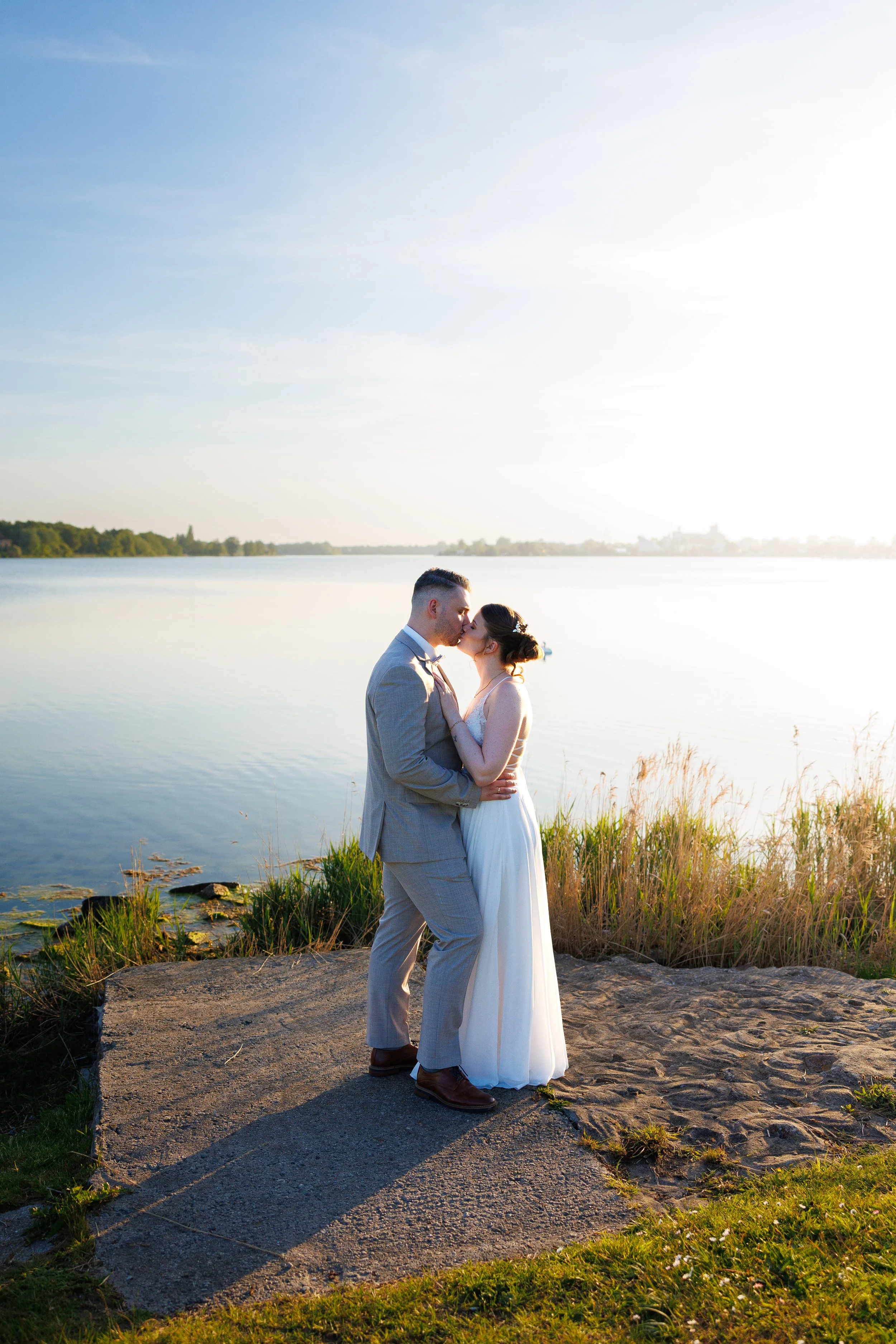 Ein Paar bei einem Hochzeitsshoot am See bei Sonnenuntergang, umarmend und sich küssten.