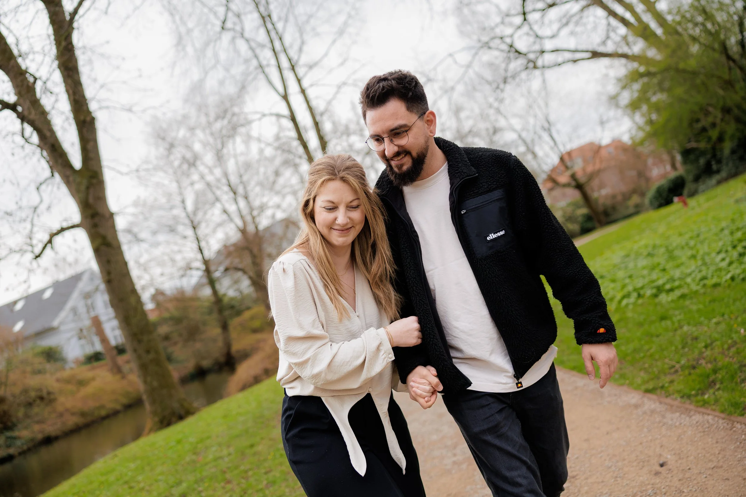 Ein Mann und eine Frau halten Händchen beim Spaziergang im Park, umgeben von Bäumen und Grünflächen.