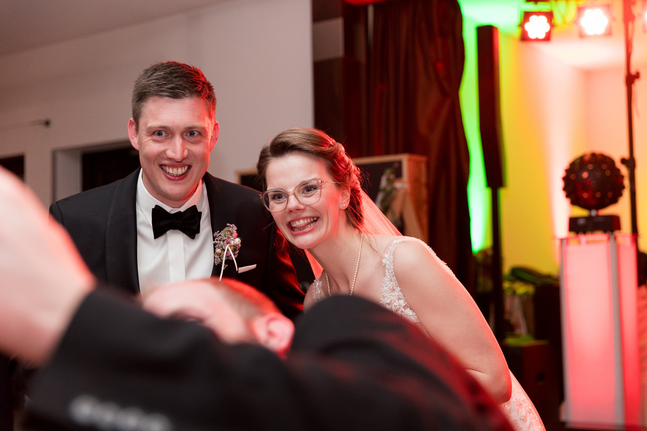 Ein glückliches Paar auf einer Hochzeitsparty, der Mann trägt einen schwarzen Anzug mit Fliege, die Frau trägt ein weißes Brautkleid und Brille.