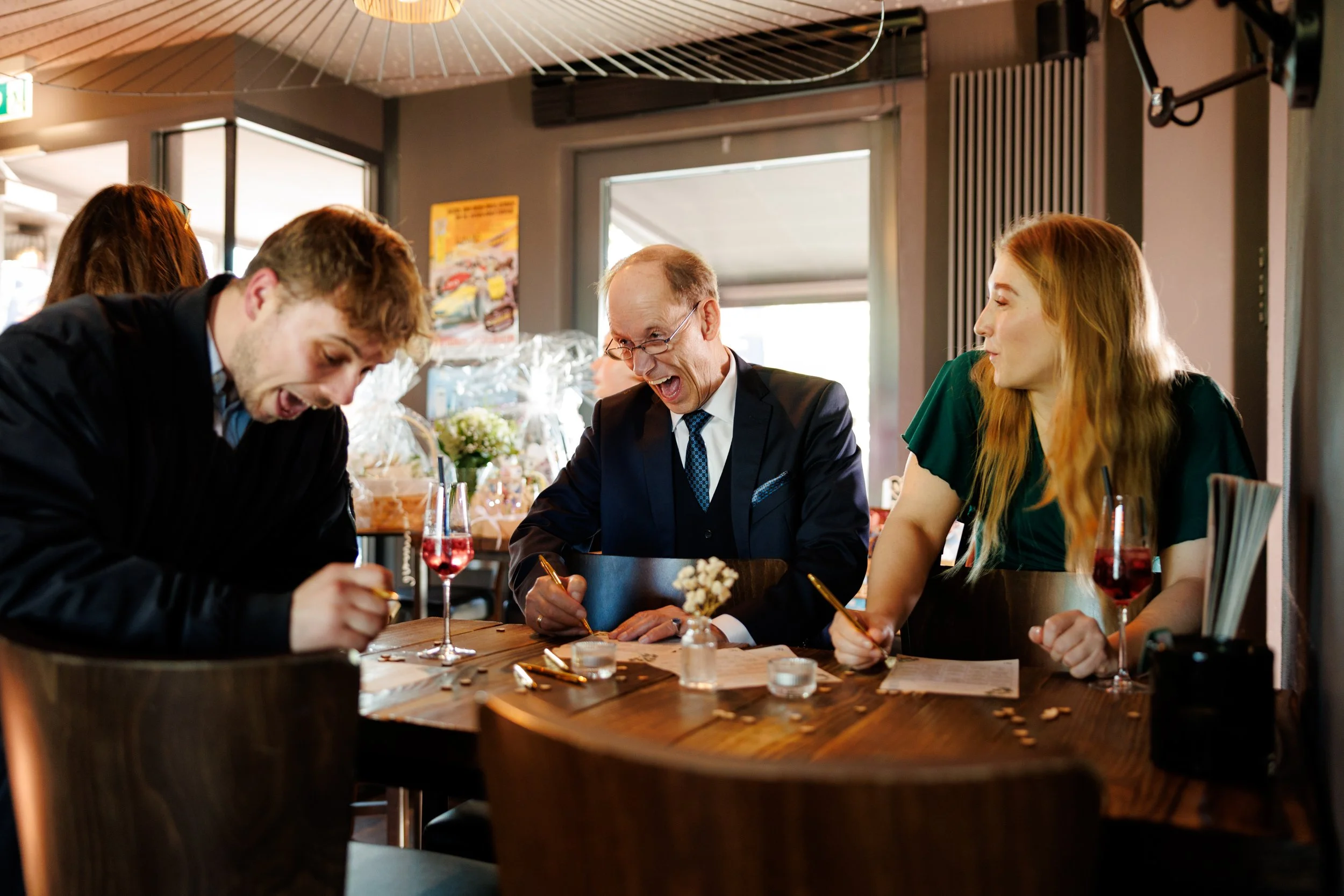 Menschen sitzen in einem Restaurant, lachen und unterhalten sich bei einem Essen, es sind Weingläser und Teller auf dem Tisch.