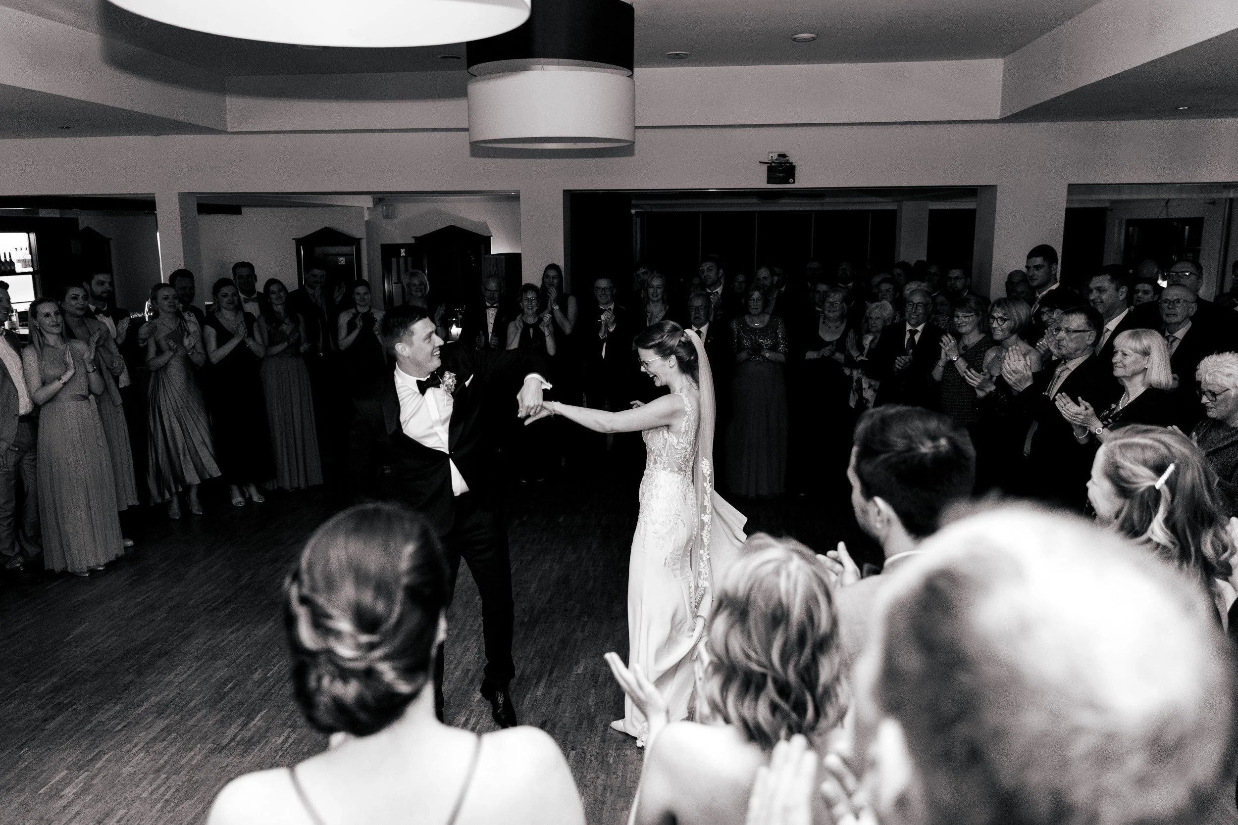Ein Brautpaar tanzt auf einer Hochzeit vor einer großen Gruppe von Gästen, die applaudieren und zuschauen.