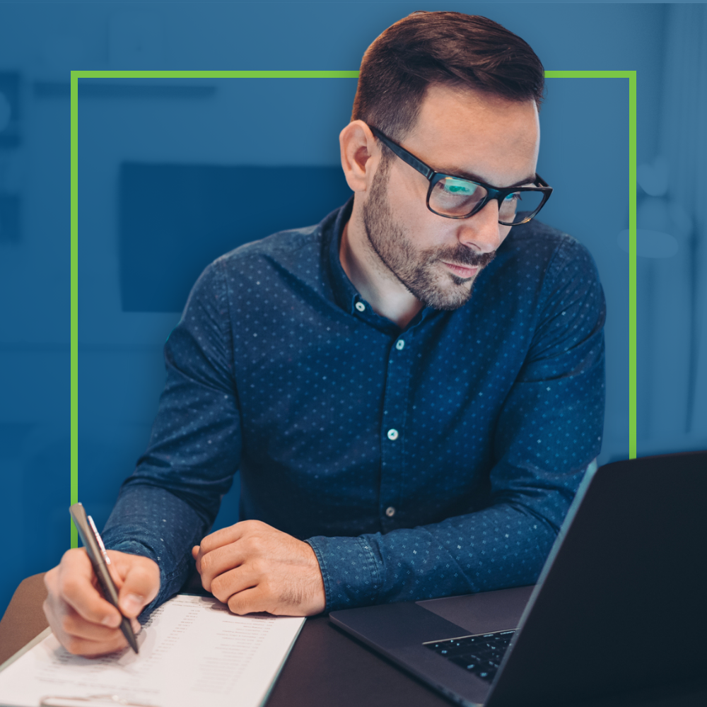 Man writing notes while working on a laptop