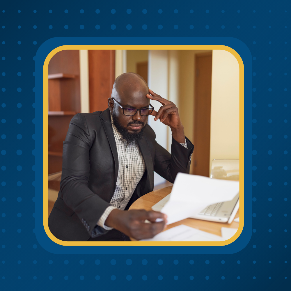 Man reviewing financial documents at a desk with his hand on his head