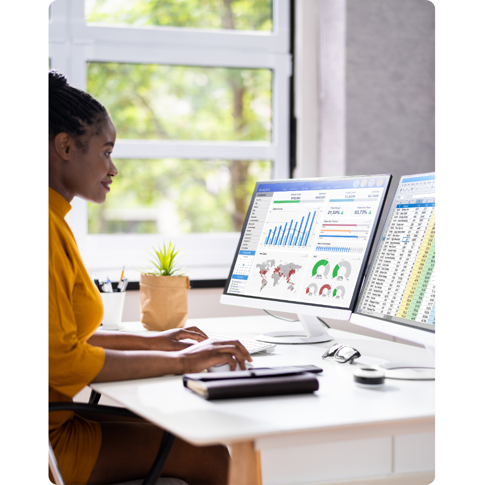 Woman working at a desk with multiple monitors showing business data