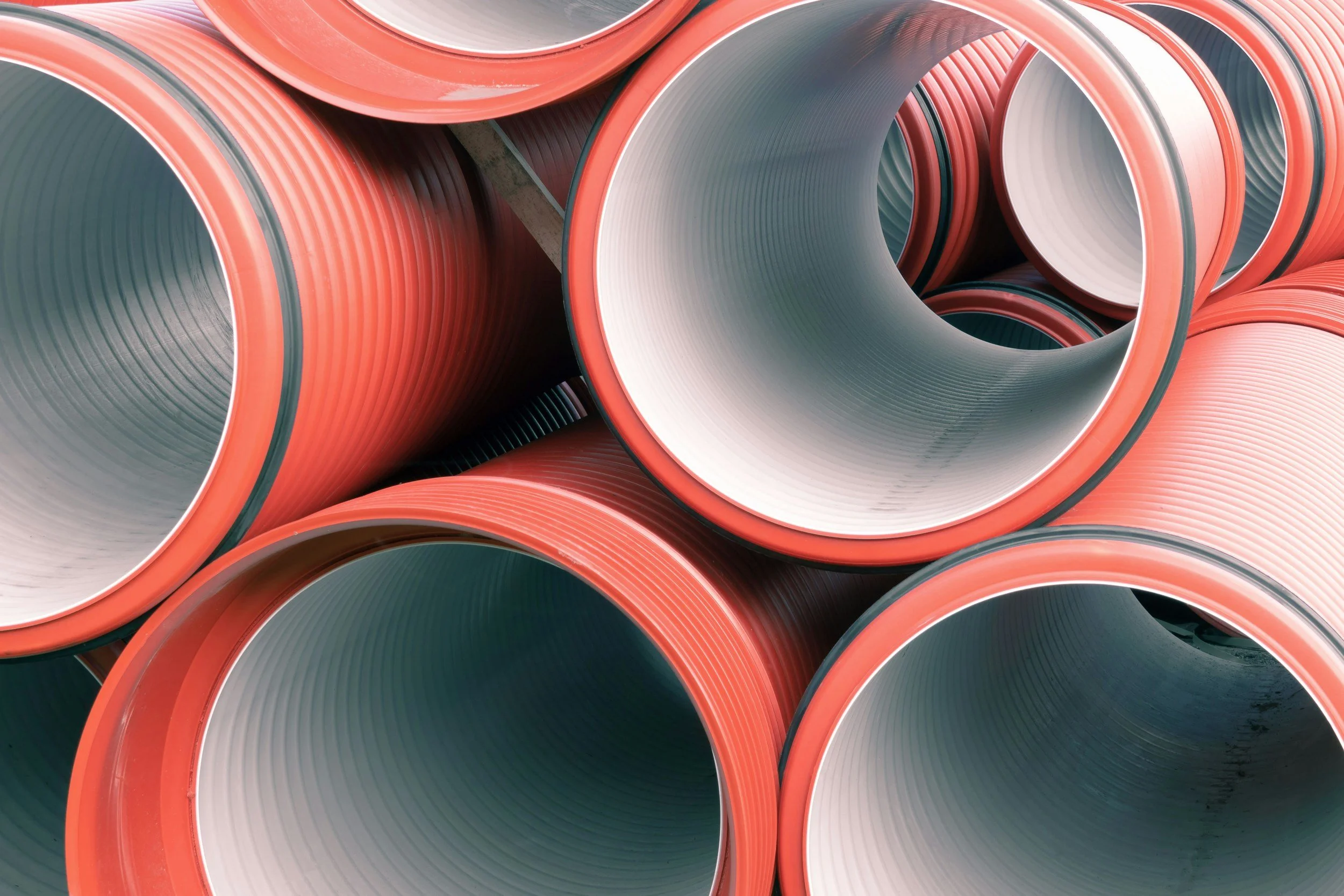 Stacked orange and white plastic pipes with smooth, ribbed inner surfaces.