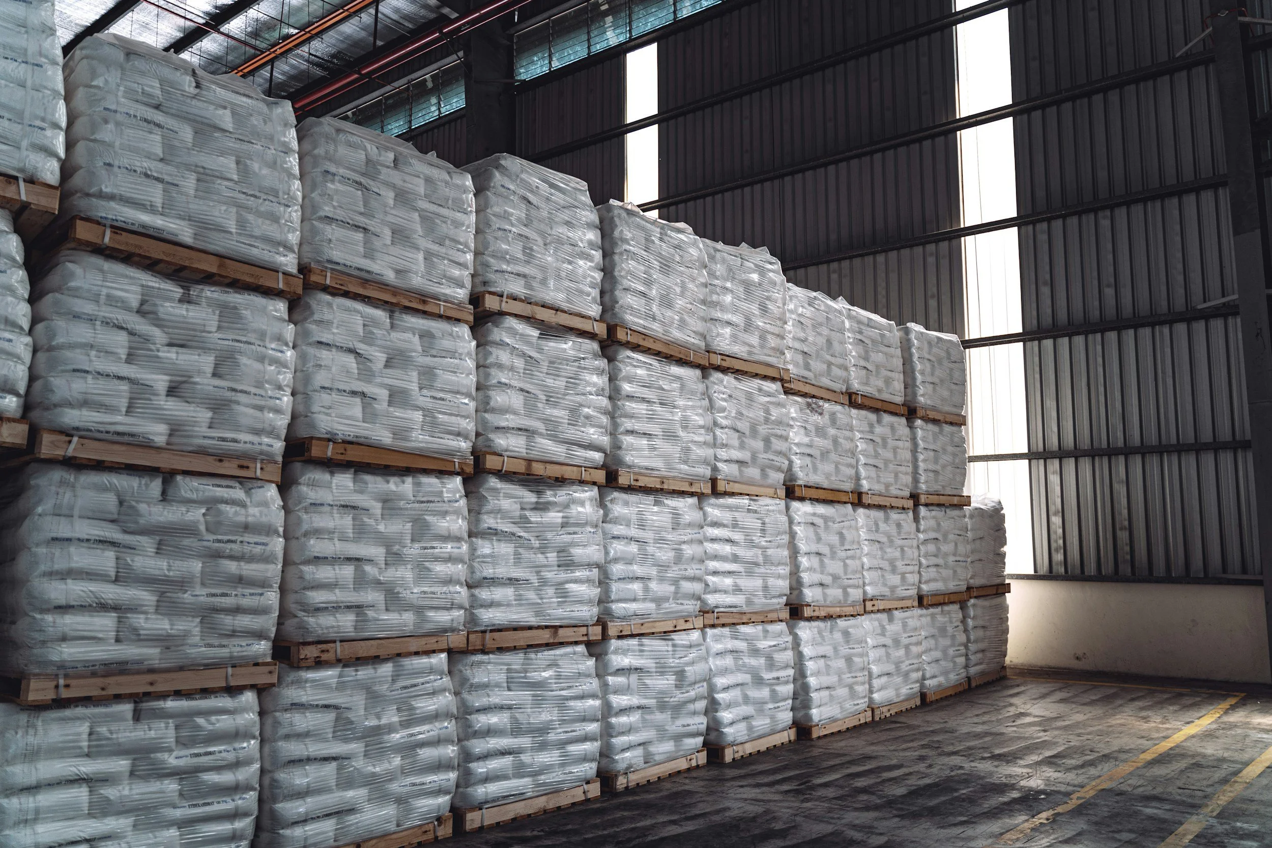 Pallets stacked with bags of what appears to be a powdered or granular substance inside a warehouse.