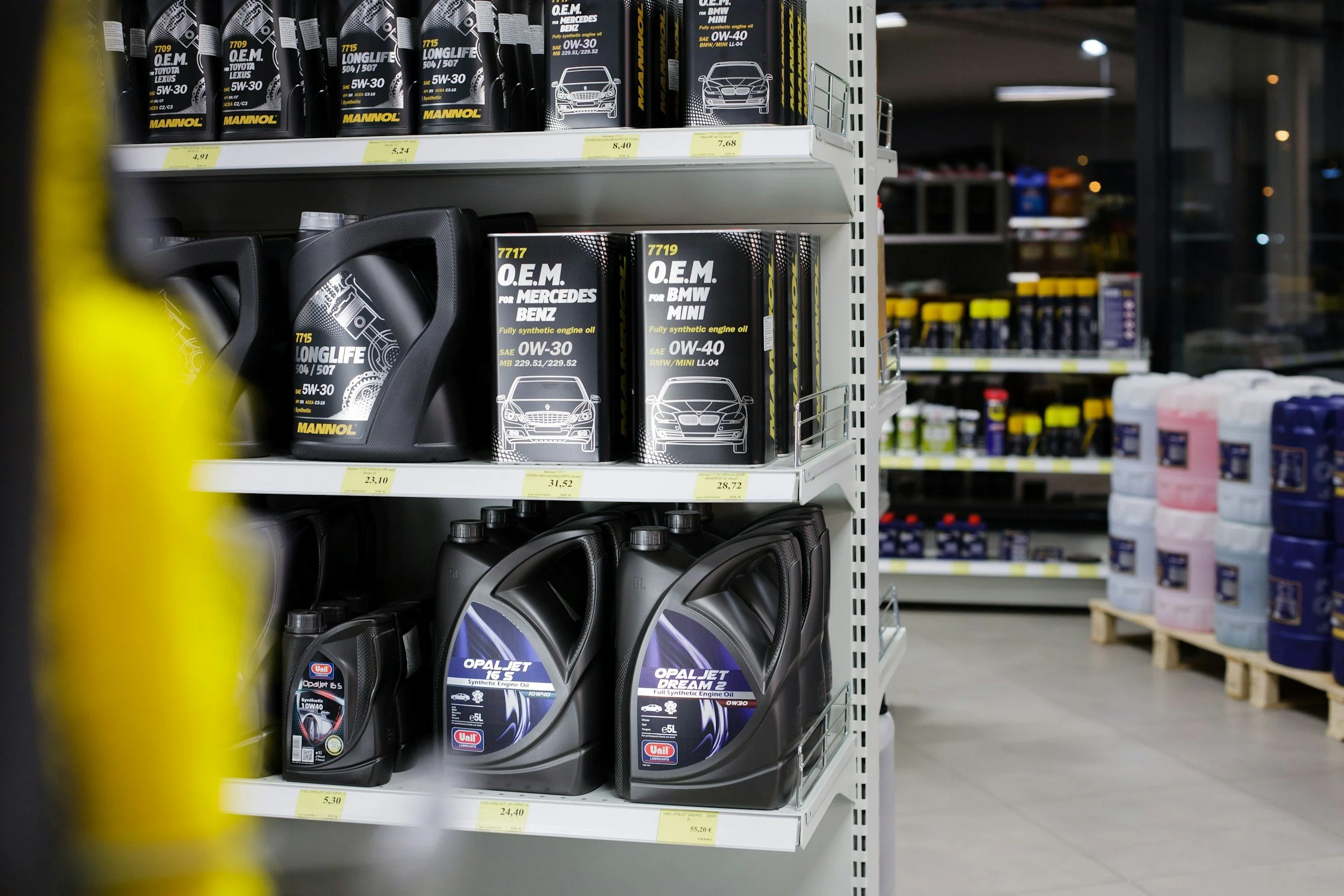 A store shelf displaying various bottles and containers of motor oil and engine oil for cars, with some products labeled for specific car brands like Mercedes, BMW, and Mini.