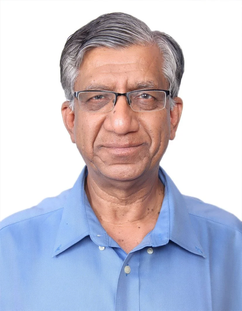 A middle-aged man with gray hair and glasses wearing a blue collared shirt, smiling gently against a plain white background.