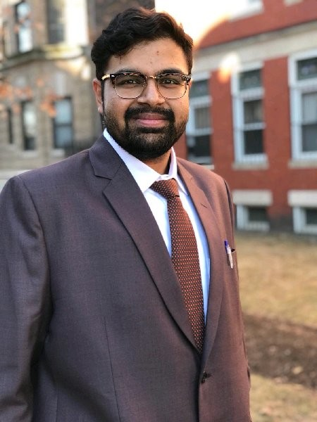 A man in a suit and tie standing outdoors in front of a residential building.