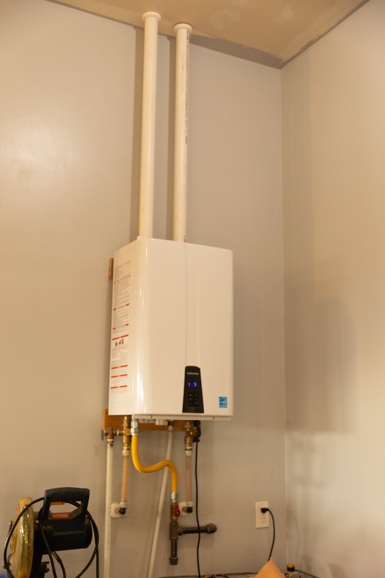 Tankless water heater installed on a wall with pipes connected, in a utility room setting.