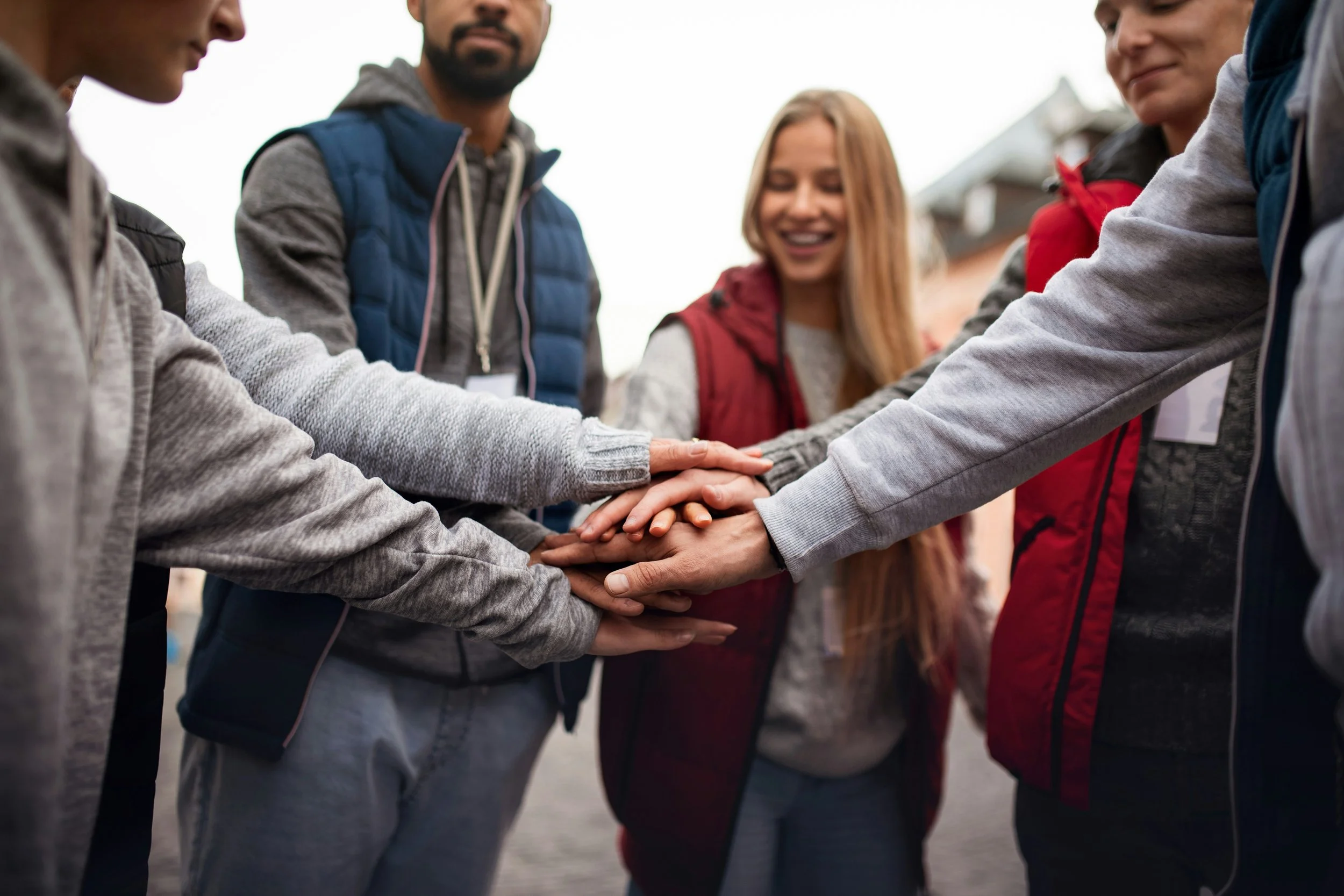 Group of diverse young people placing their hands together in a gesture of unity outdoors.