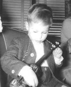 Black and white photo of a young boy in a jacket holding and playing with a musical instrument.