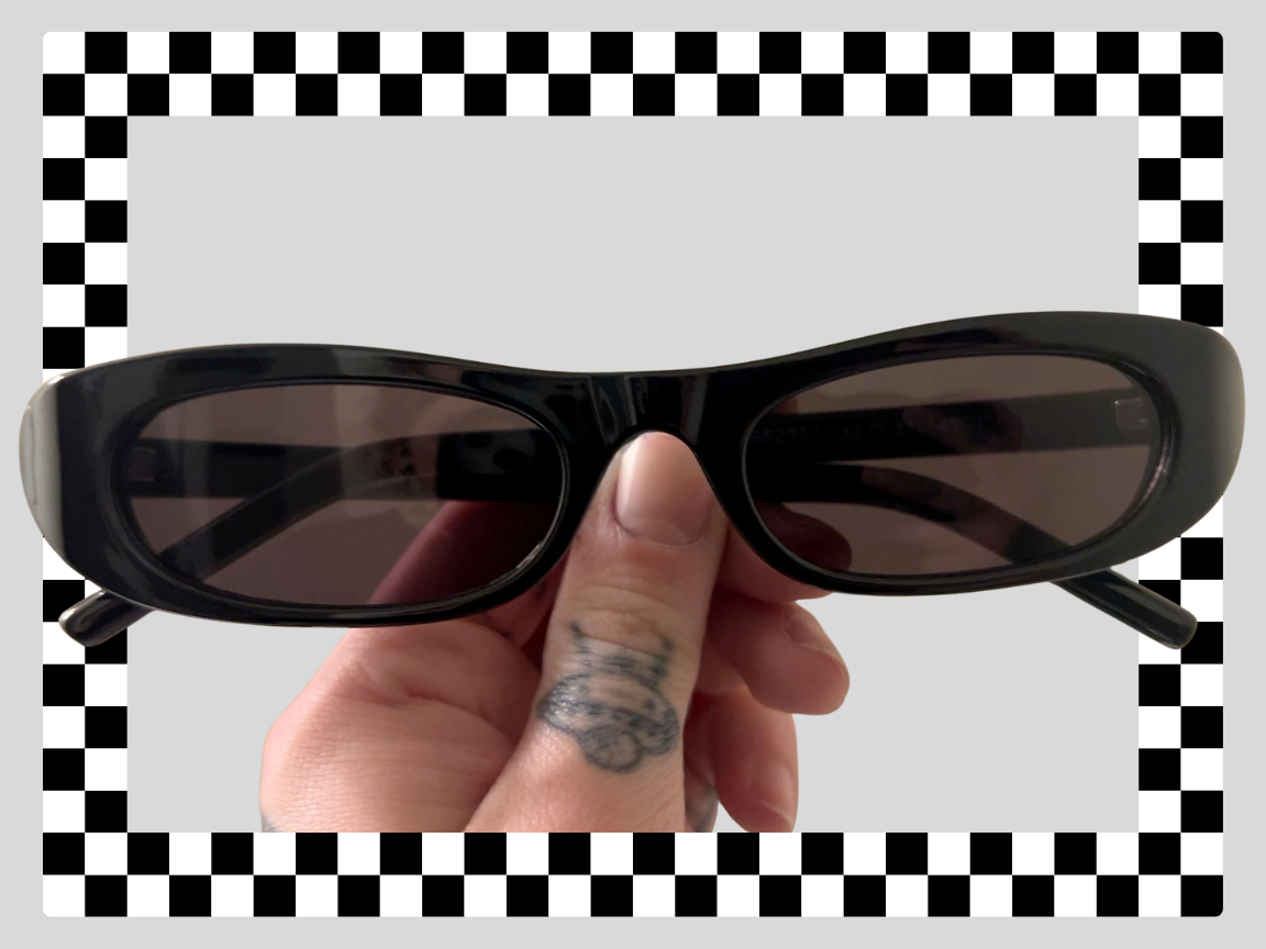 A person holding black sunglasses with rectangular lenses, against a checkered and light gray background.