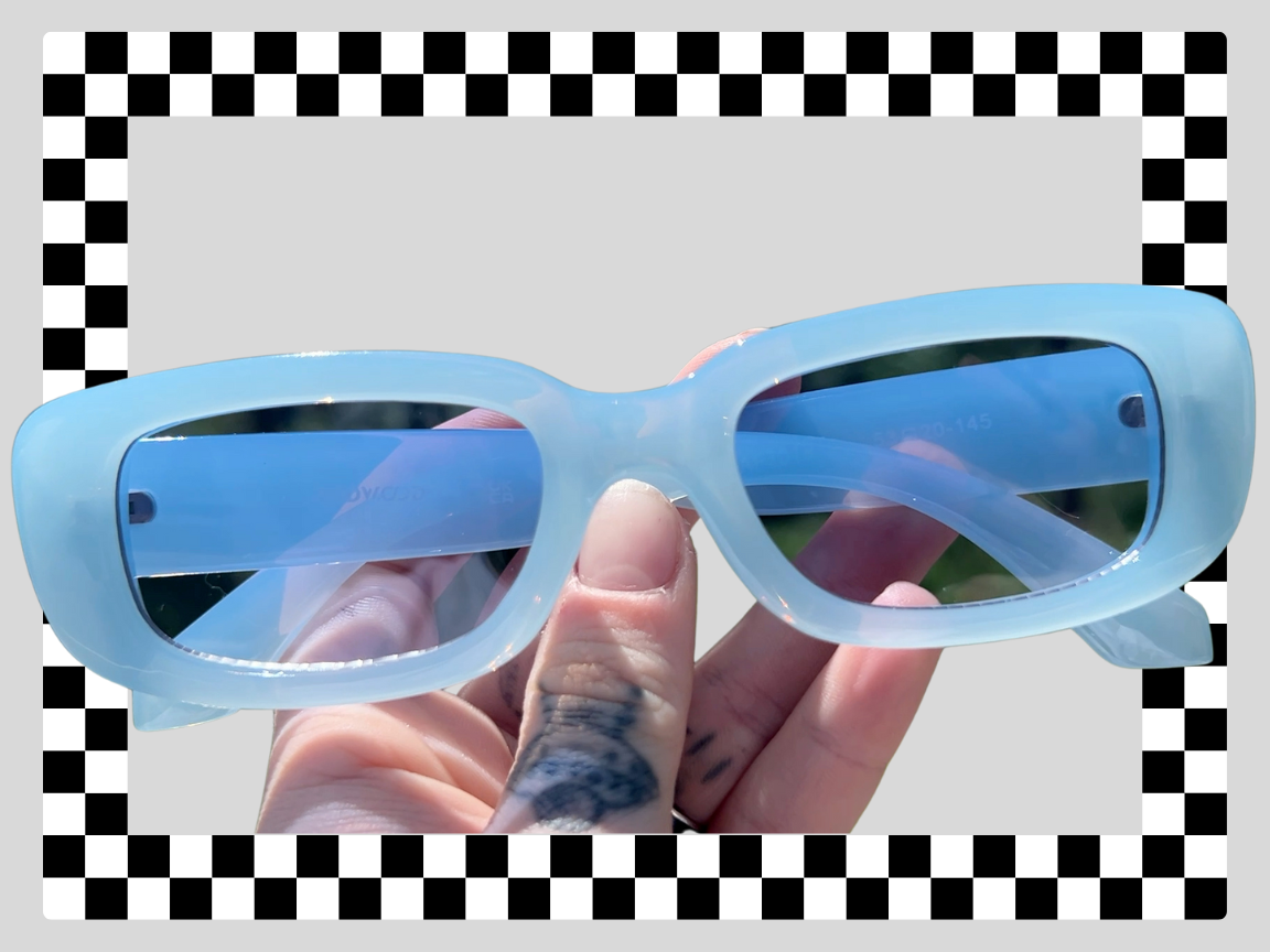 A person holding a pair of cloudy blue sunglasses outdoors, with a checkered border and a plain gray background.
