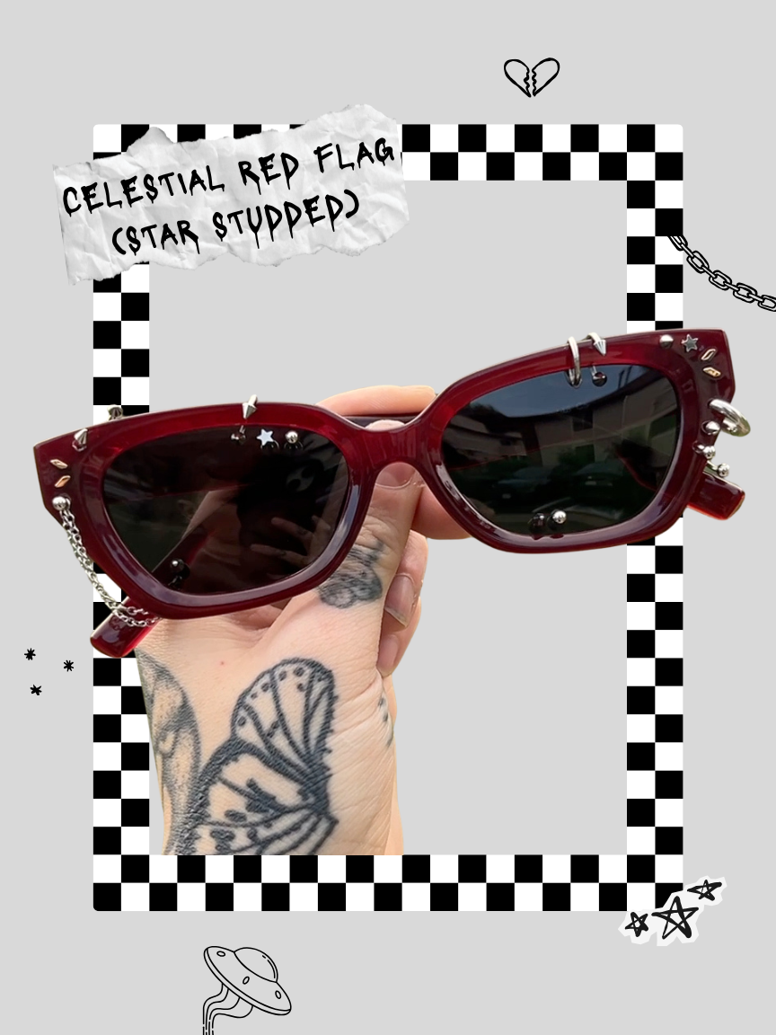 Hand with tattoos holding a pair of red sunglasses with jewelry adornments around a Creative Commons-themed, checkered frame, with decorative doodles, including a broken heart, stars, and a UFO, and a torn label reading 'Celestial Red Flag (Star Stumped)'.