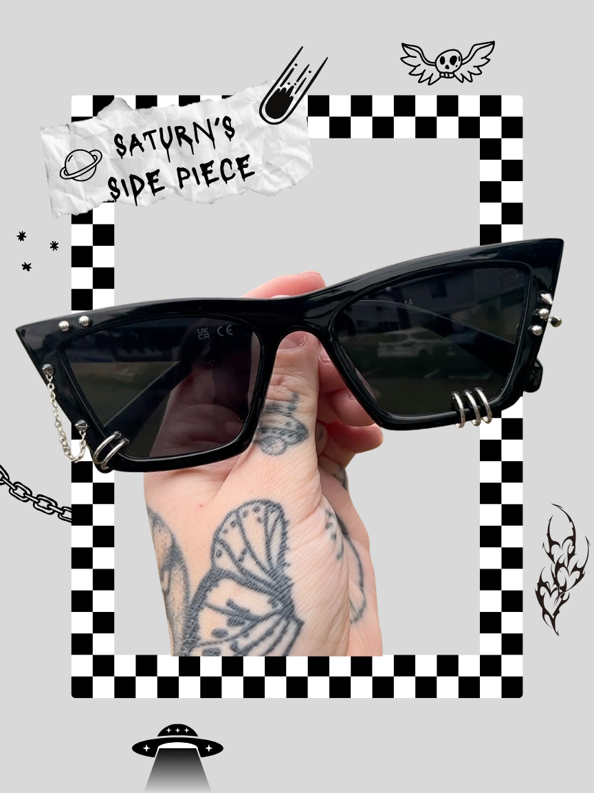 Hand holding black sunglasses with silver embellishments and chain, surrounded by graphic space-themed and gothic doodles on a gray background.