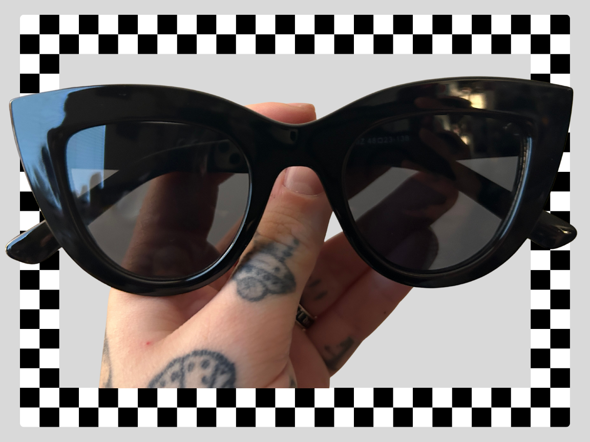 A person holding black sunglasses with a checkered pattern background.