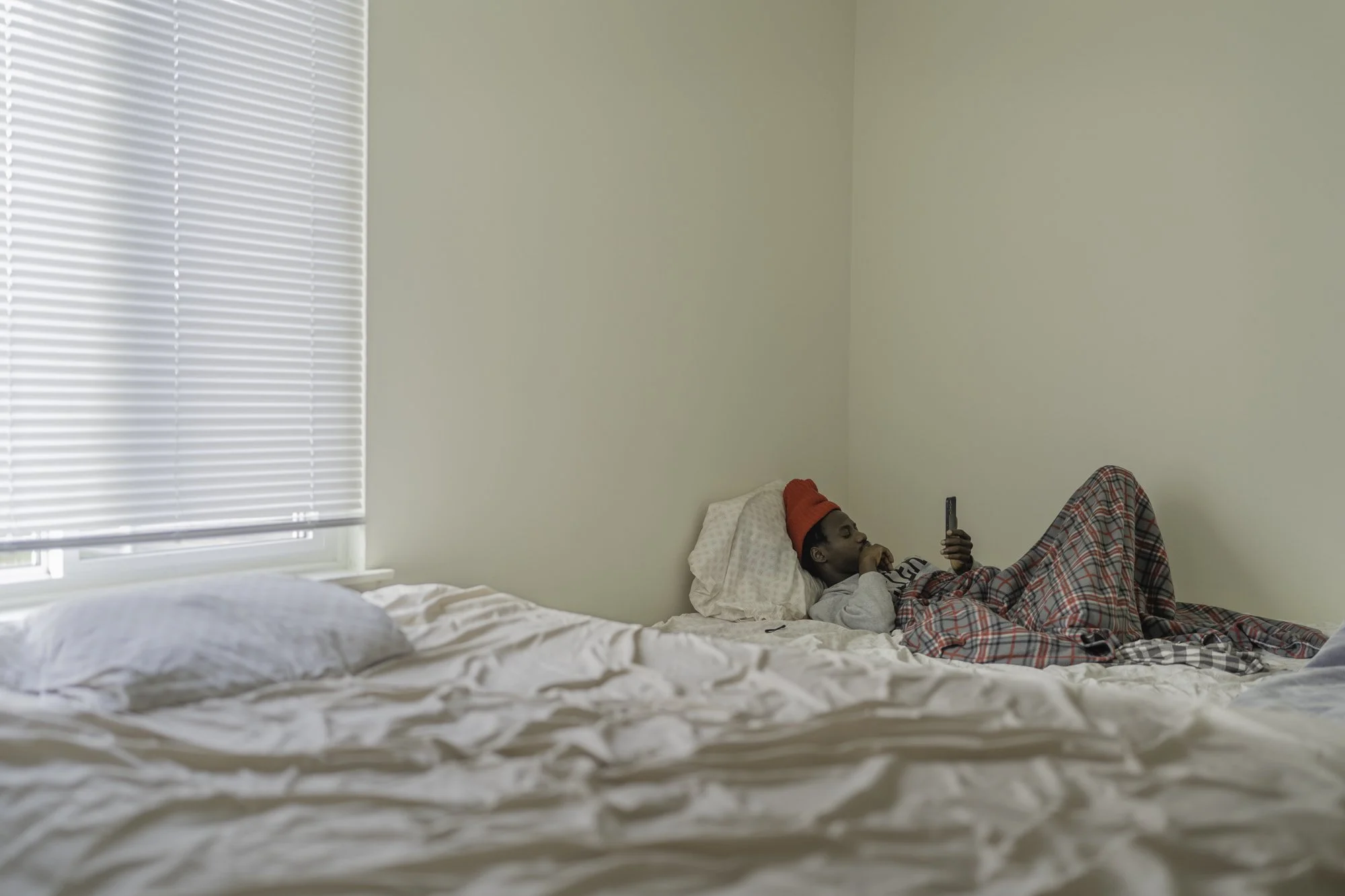 Michigan — A Baye Fall man who asks not to be identified sits in the bedroom he shares with three others in Michigan on Saturday, December 28, 2024. He previously lived in New York’s shelter system and says having his own space made him realize how d