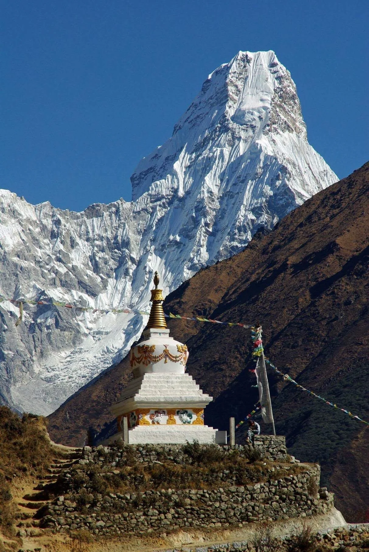 Snöklätt berg i Himalaya med en tibetansk stupa i förgrunden, omgivet av berg och en klar blå himmel.