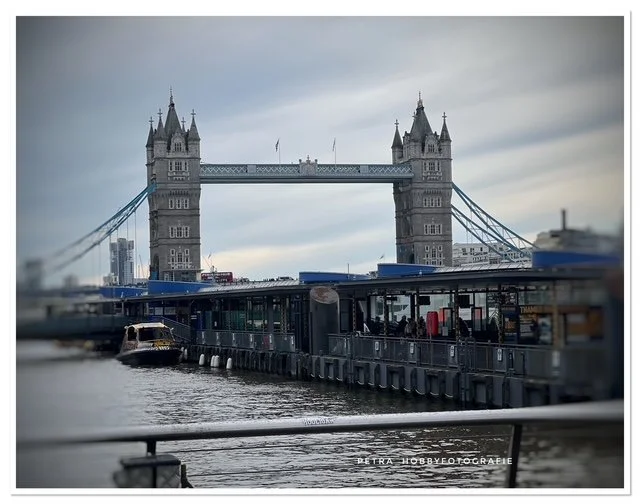 The Tower Bridge over the River Thames in London with boats and a viewing platform in the foreground.