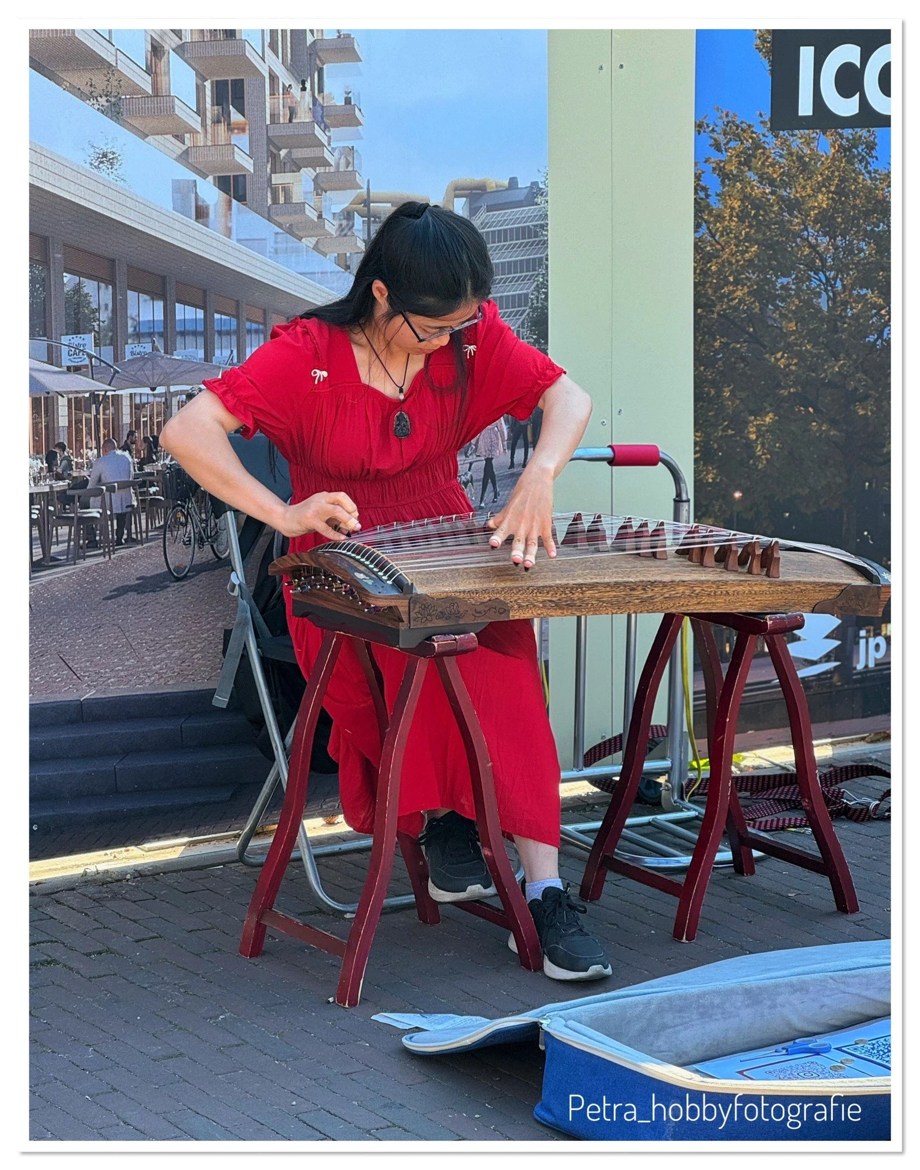 Woman in a red dress plays a hammered dulcimer outdoors on a sunny day.