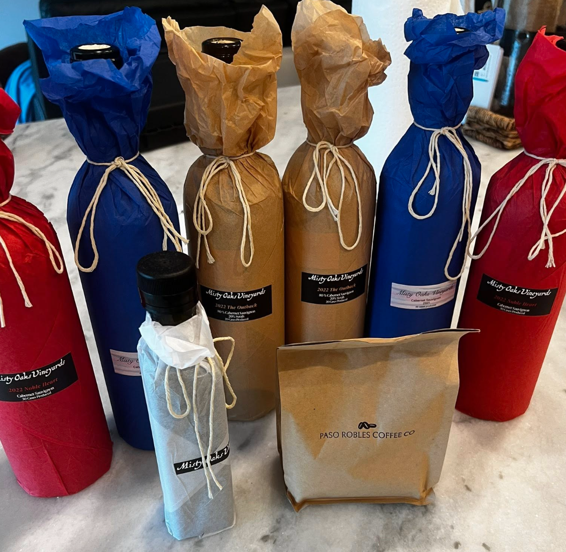 Several bottles wrapped in paper and tied with twine, along with a bag of coffee beans from Paso Robles Coffee Co., on a marble countertop.