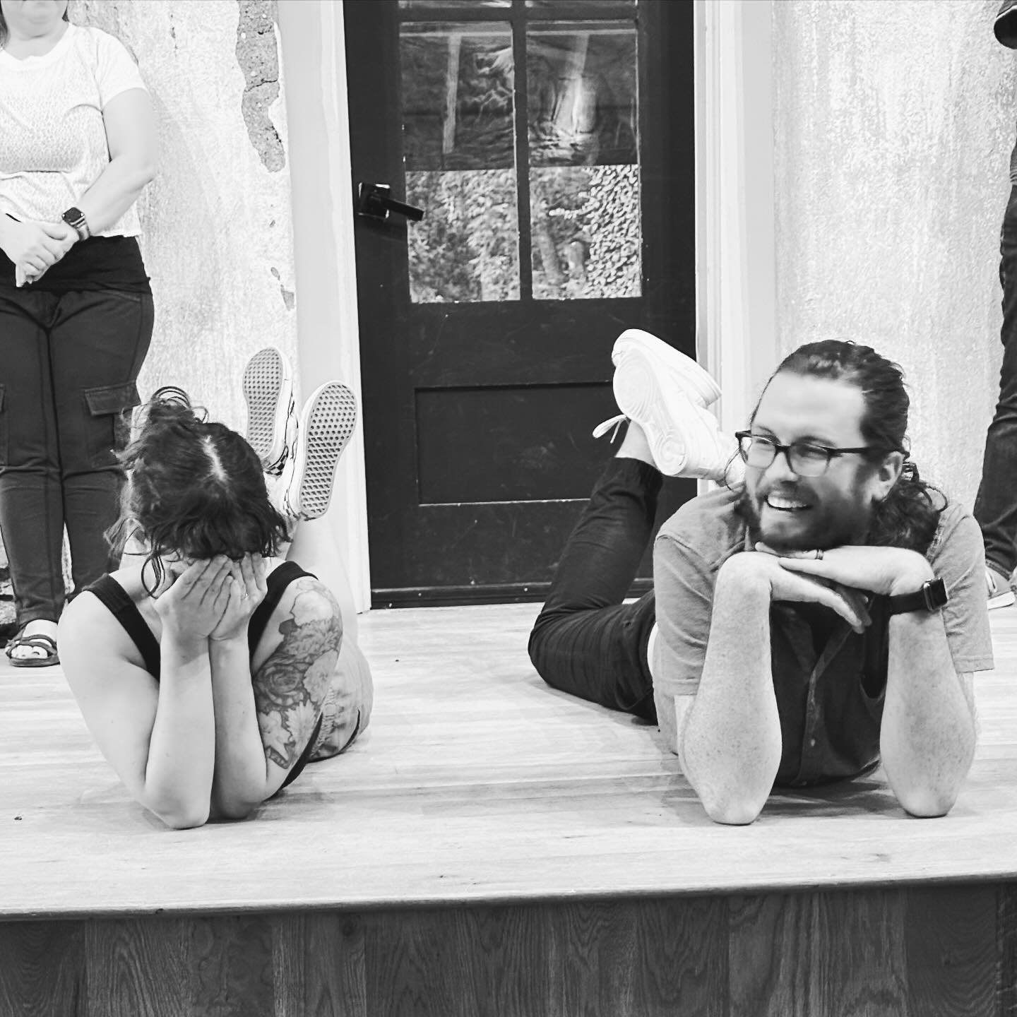 A woman with tattoos and dark hair covering her face with her hands, lying on her stomach on the floor. Improv class Charlottesville comedy Decipher Potter's fun date night Bent Theatre