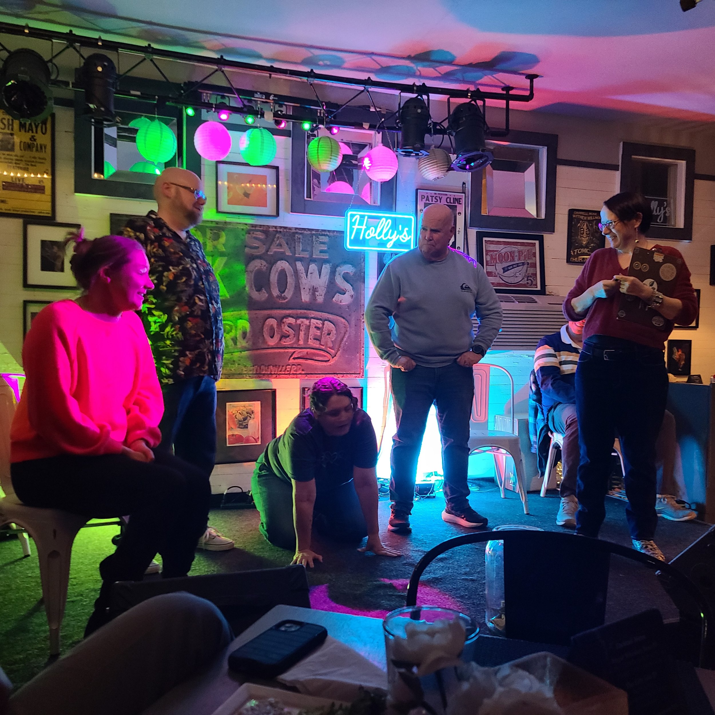 Group of people performing a game or skit on a small stage inside a lively bar. Improv class Charlottesville comedy Decipher Potter's fun date night Bent Theatre Holly's diner