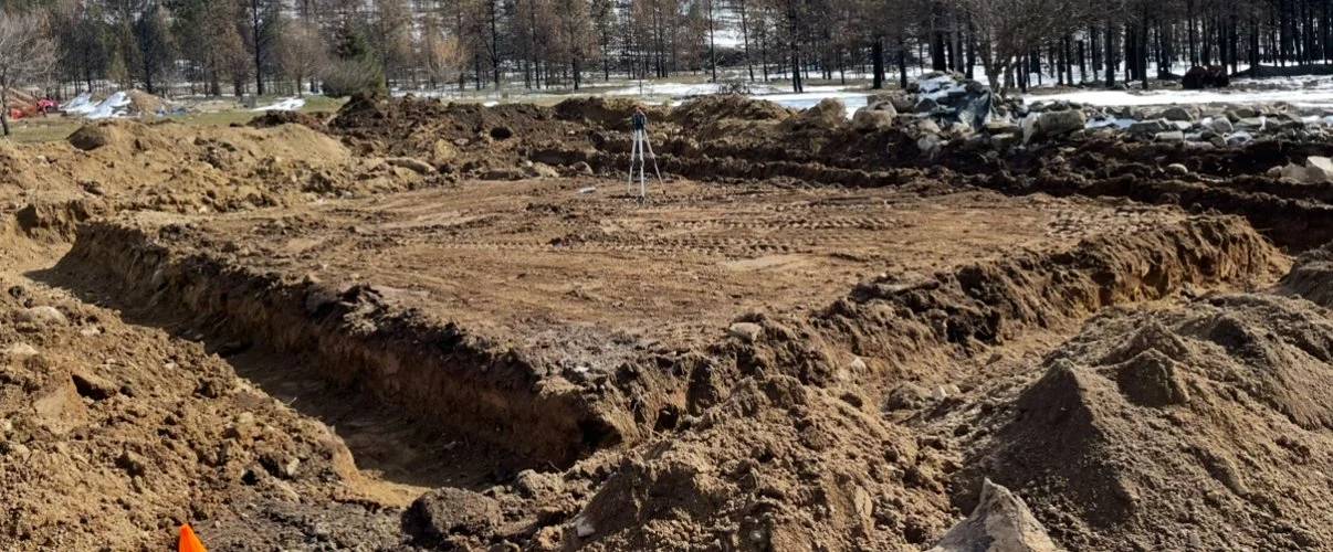 Construction site with excavated dirt, a concrete foundation, and a tripod level.