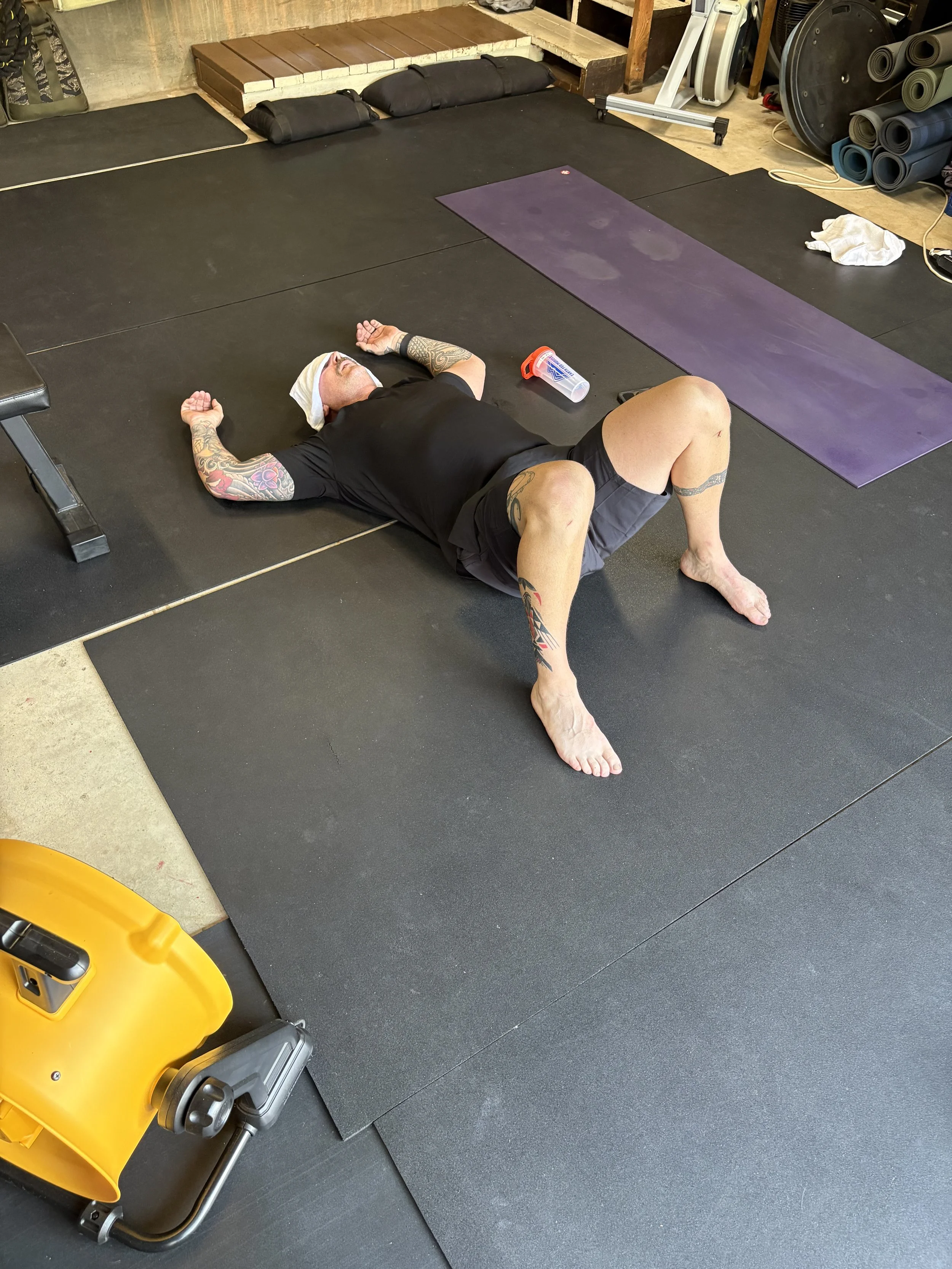 People exercising in a home gym with weightlifting and stability ball, open garage door revealing outside view.