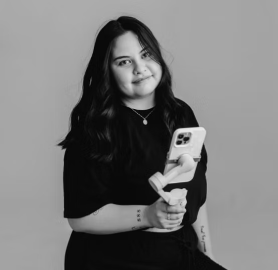 Woman with long dark hair holding a smartphone on a stabilizer, wearing a black outfit.