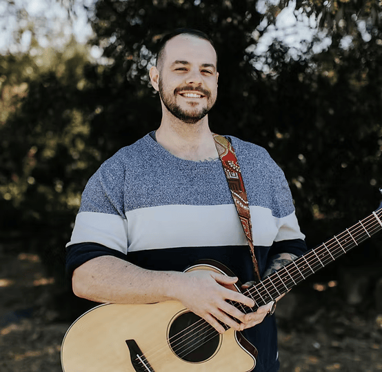 Man smiling while holding an acoustic guitar outdoors