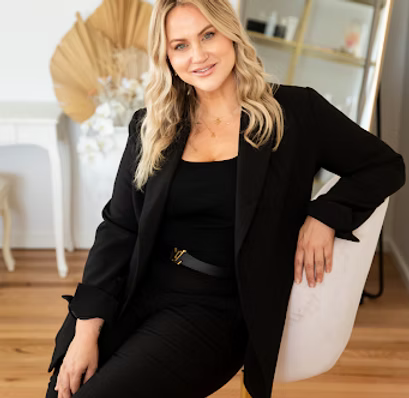Woman in black outfit sitting on a chair in a stylish interior with wooden floor and decorative elements.