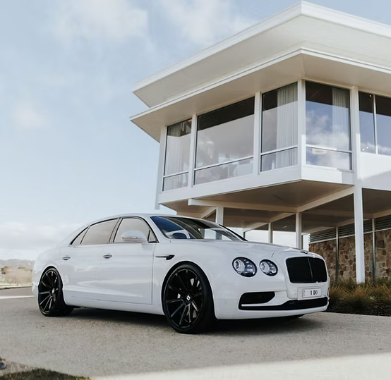 White luxury car parked in front of a modern house with large windows.
