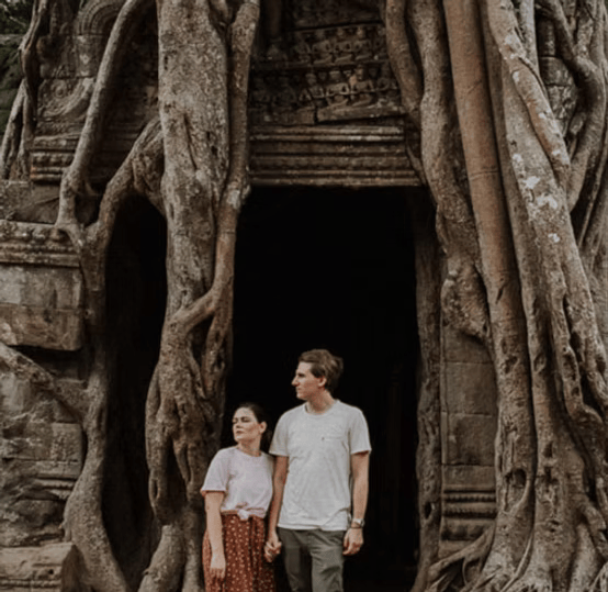 Couple standing in front of a tree-covered ancient temple entrance