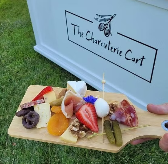 Small charcuterie board with meats, cheeses, a strawberry, pickles, apricot slices, chocolate-covered pretzel, and edible flower.