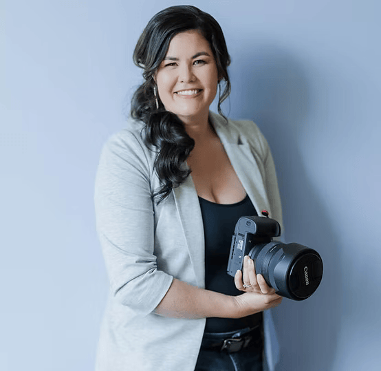 Smiling person holding a Canon camera against a light blue background.