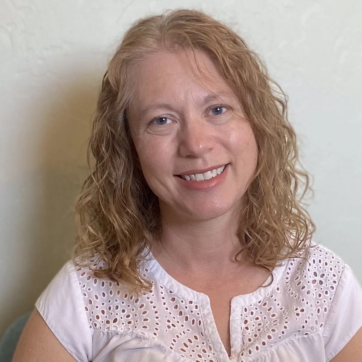 A woman, Bonnie Ledford CNM, with curly red hair smiling at the camera, wearing a white blouse with eyelet details.