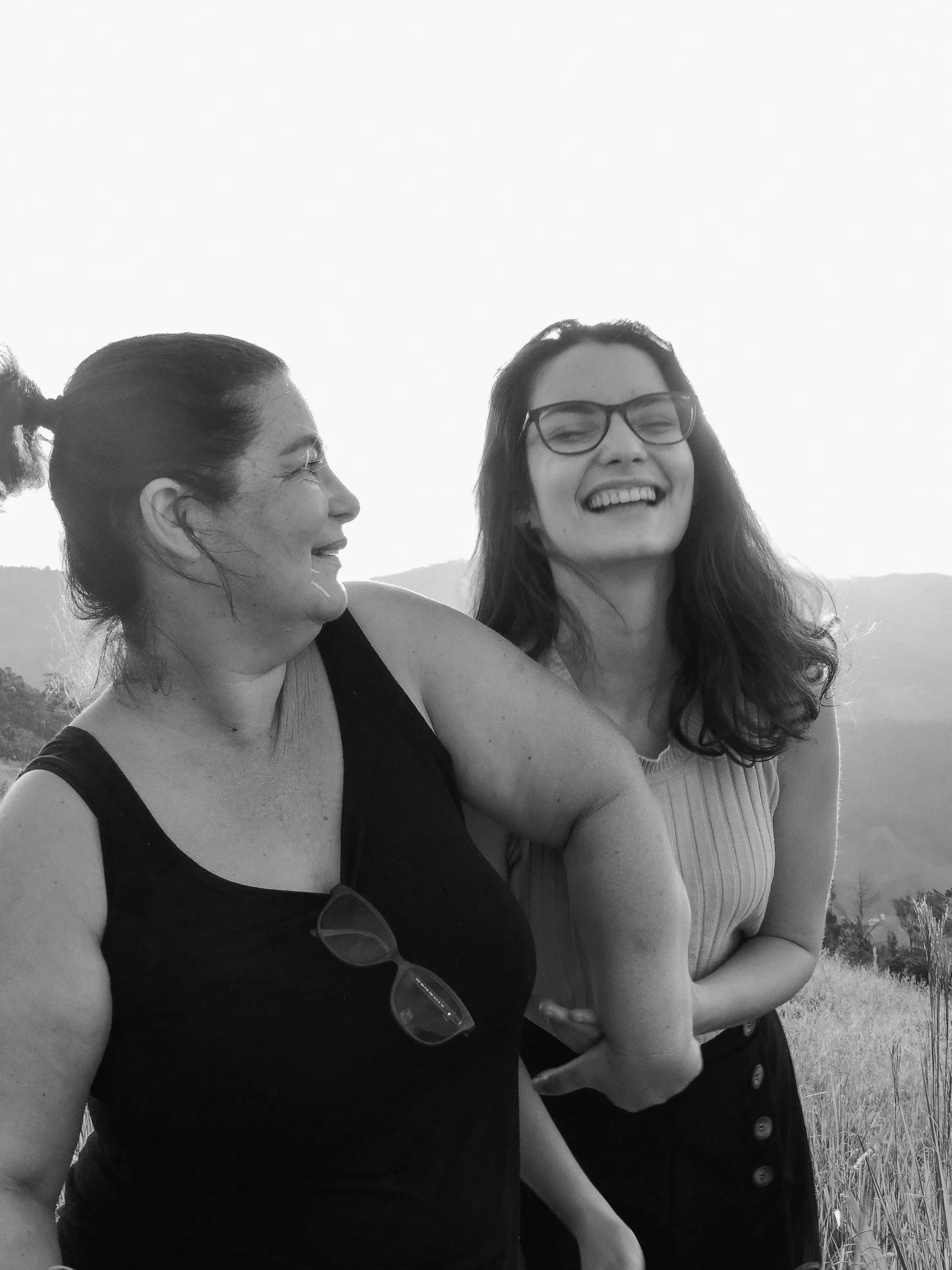 Two women laughing outdoors with a scenic mountain landscape in the background