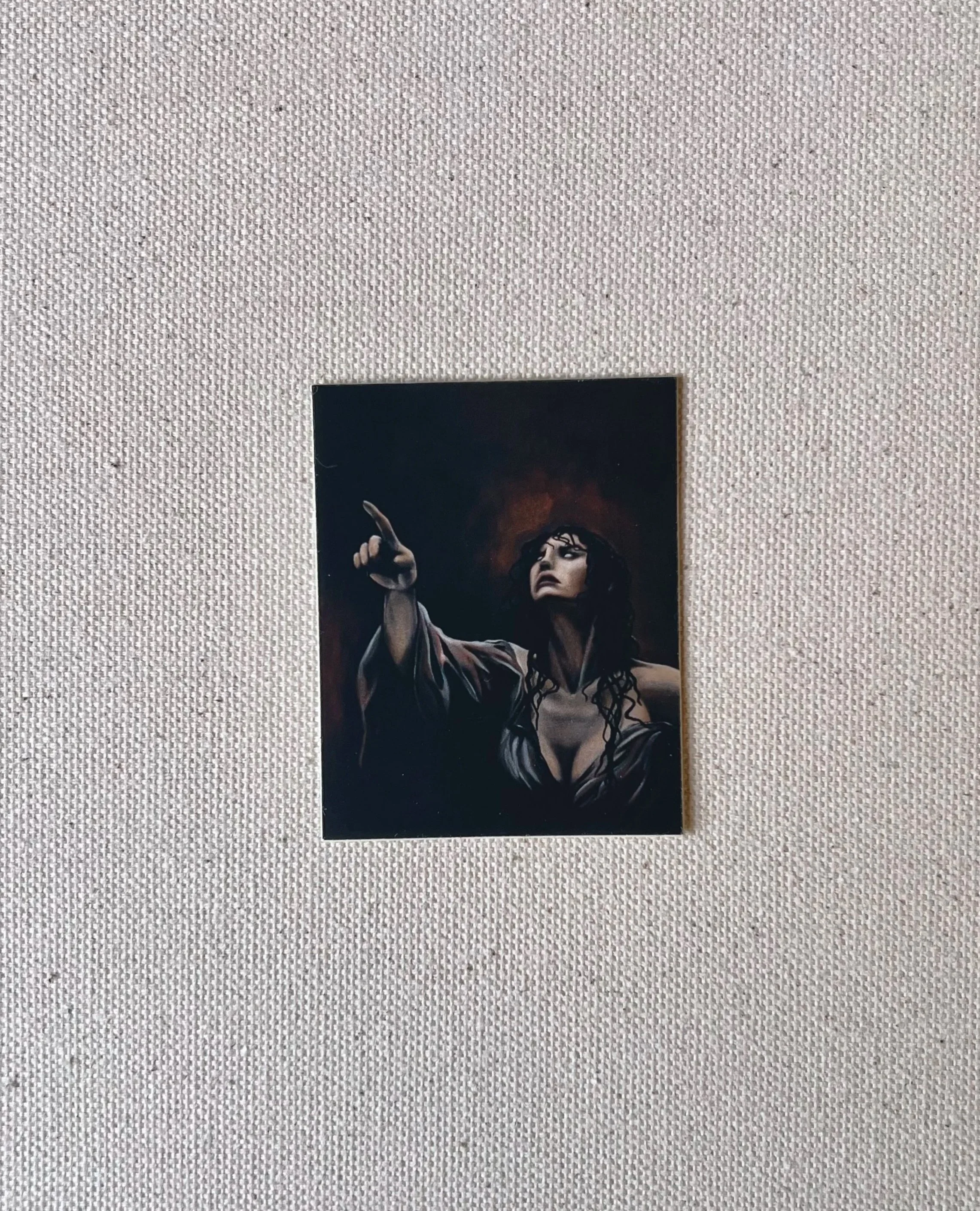 A sticker featuring an oil painting of a dark haired woman pointing towards the upper left corner, set against a dark background