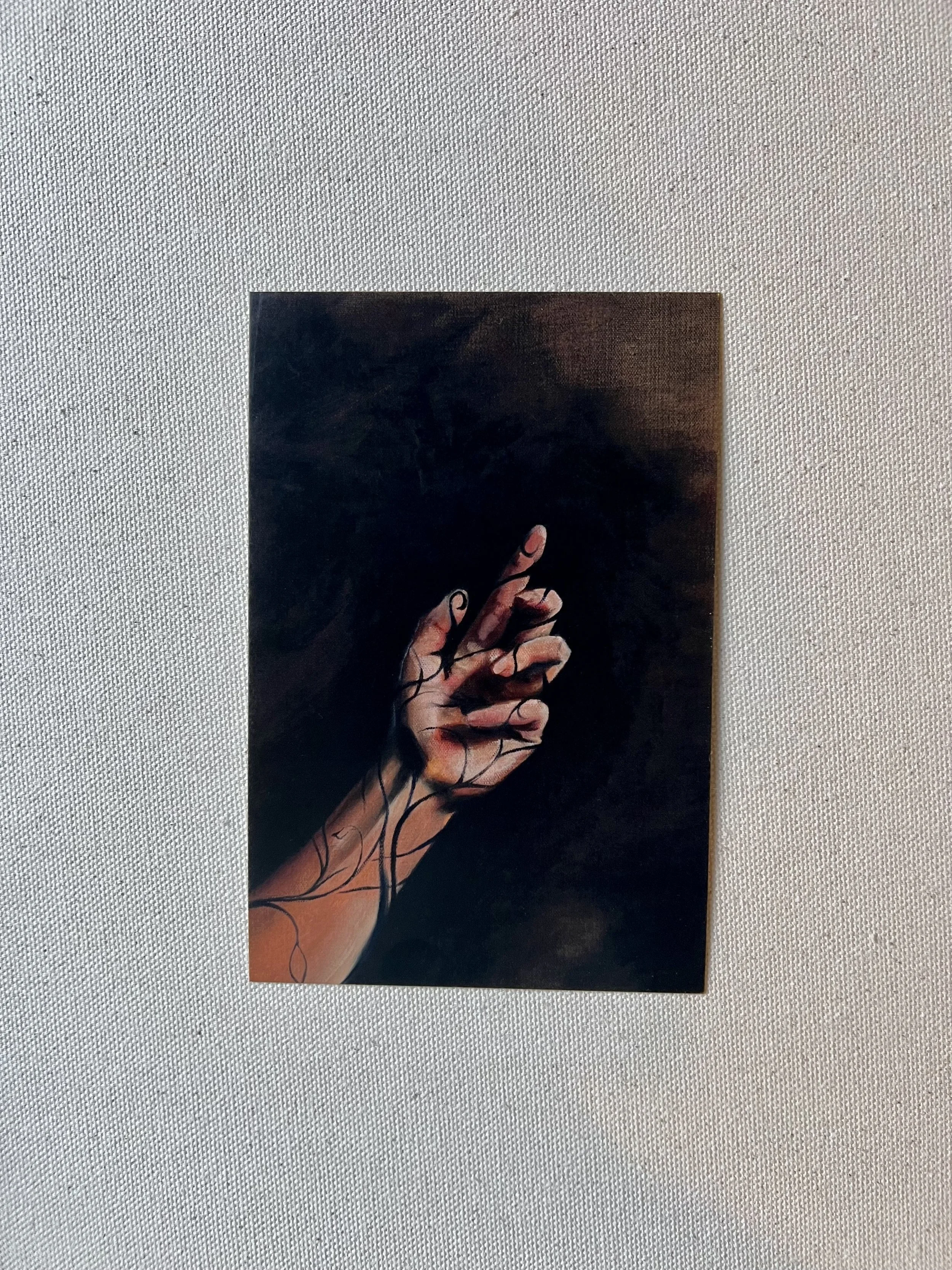 Front of a postcard featuring an oil painting of a hand set against a dark background