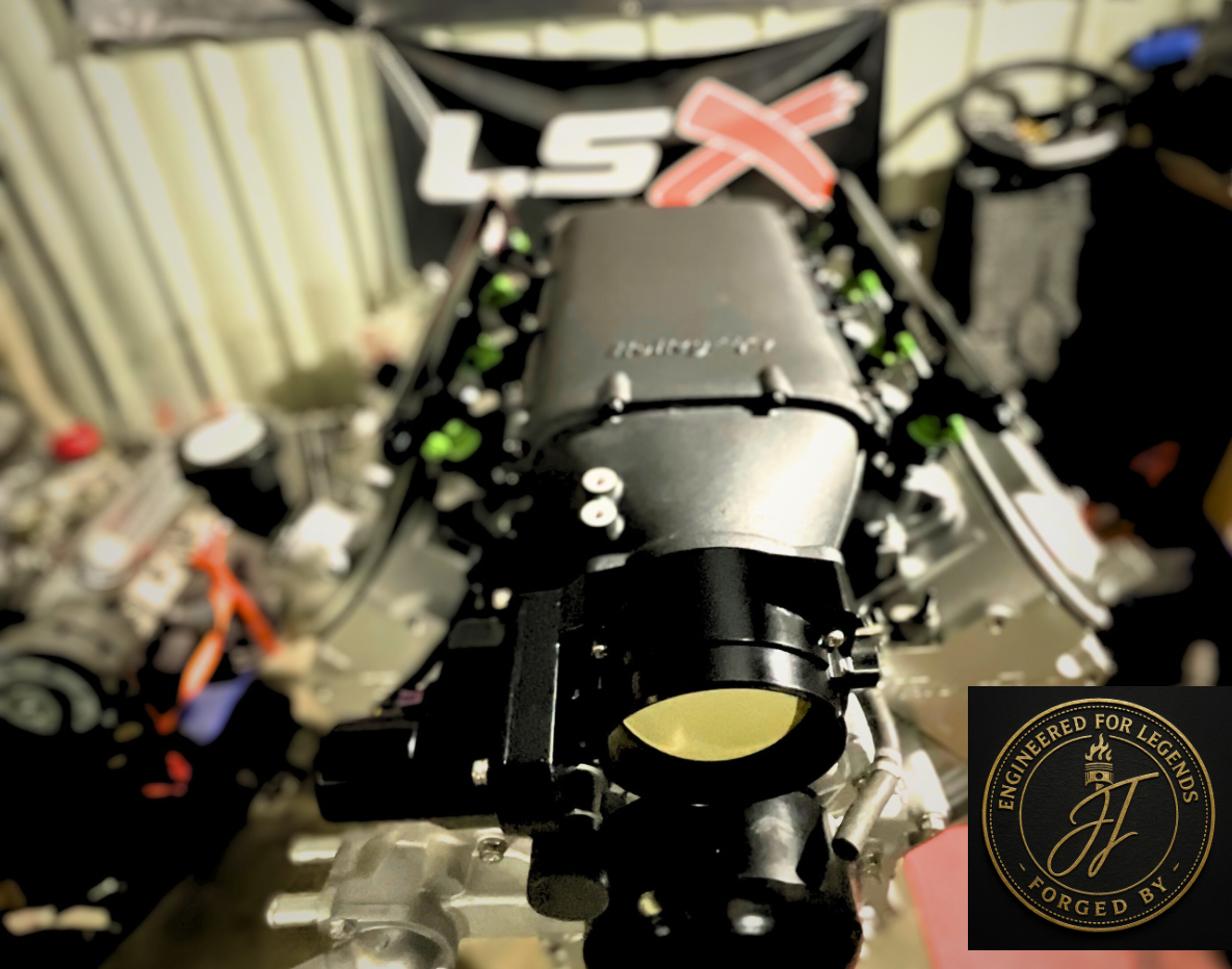 Close-up of an LSX engine with a black intake manifold in a garage, focusing on the throttle body. Inset shows a logo with the text 'Engineered for Legends, Forged By' and stylized initials.