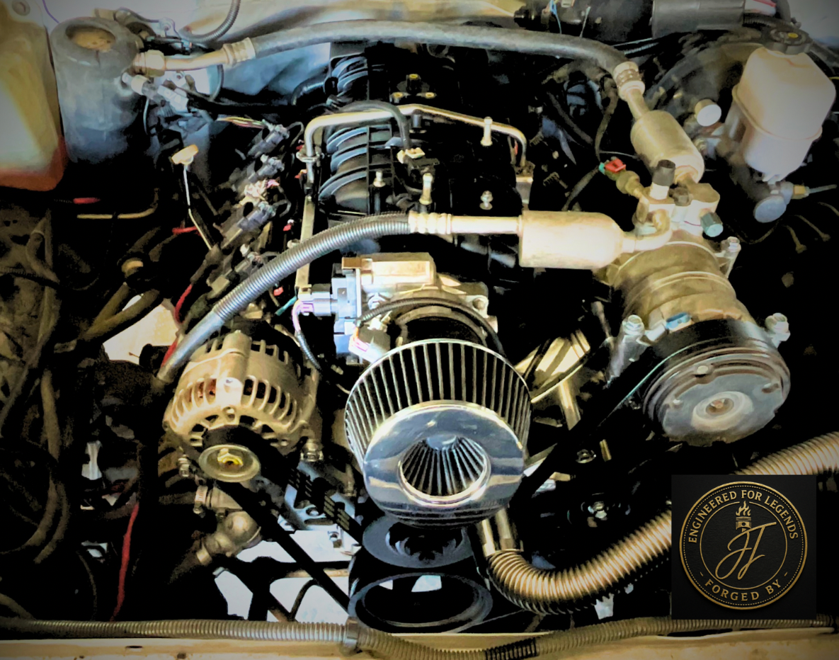 Close-up of a car engine with visible air intake, alternator, and various components, featuring a logo with 'Engineered for Legends Forged by JJ'.