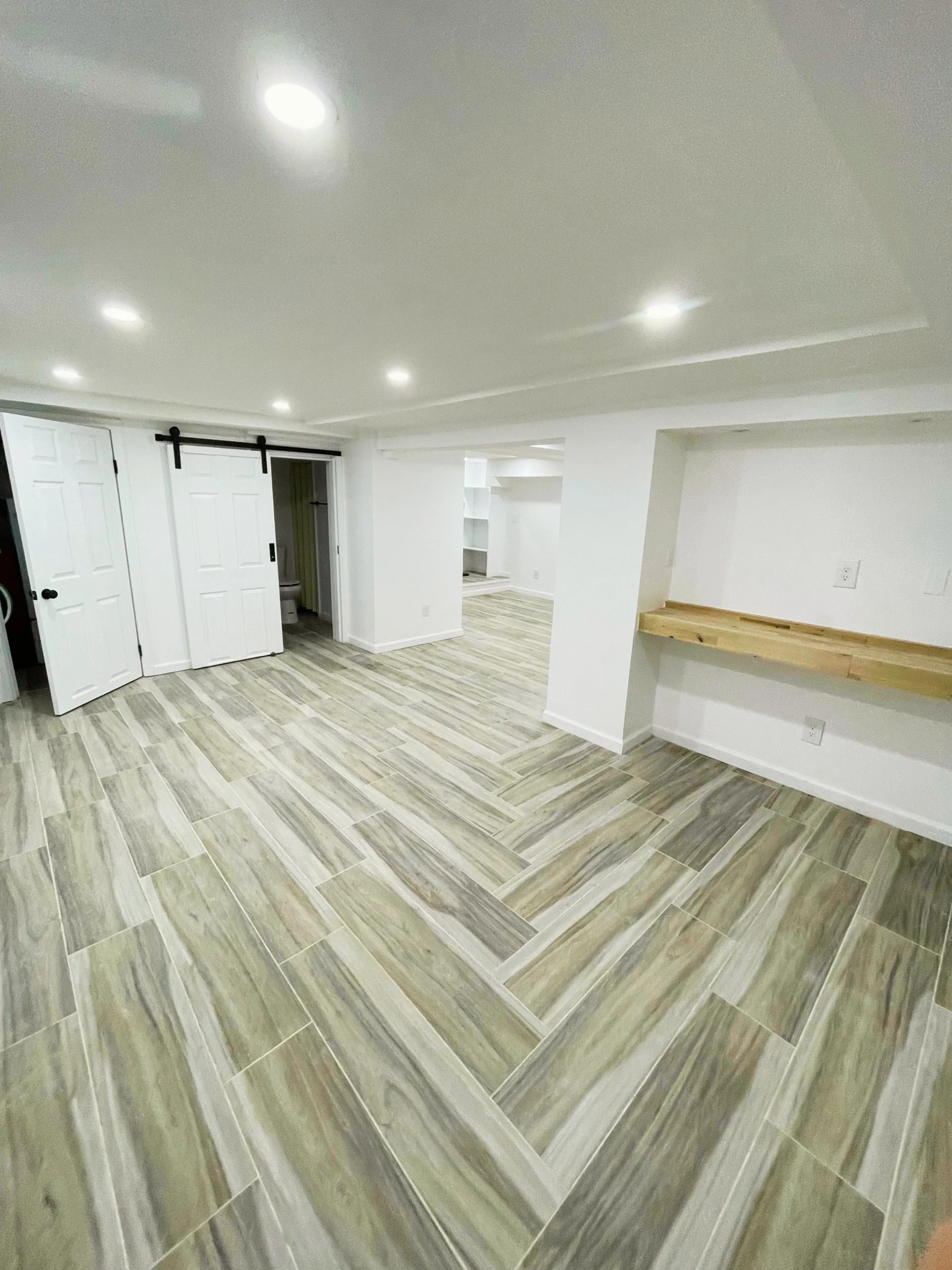 Empty room with wood-look tile flooring, white walls, ceiling with built-in lights, two white doors, and a small open closet area.