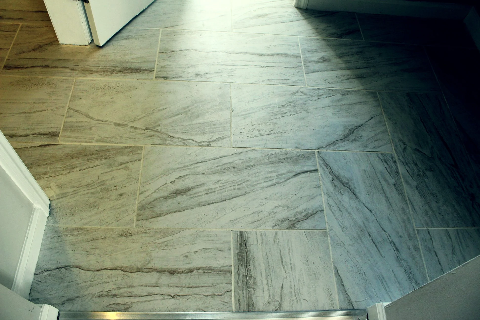 Close-up of marble-patterned tile flooring in a room, with part of a doorway and baseboard visible.