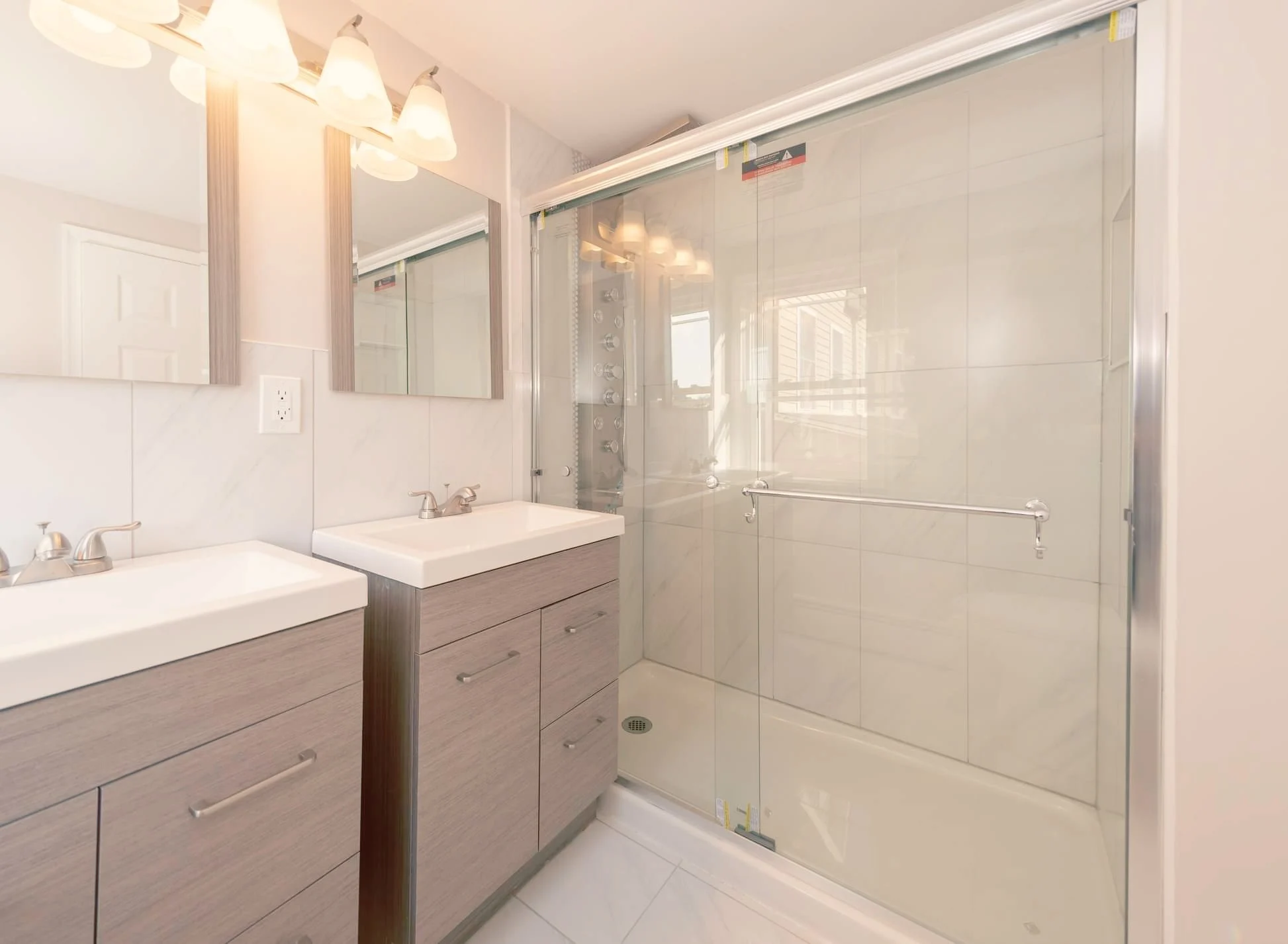 Bathroom with two sinks, mirrors, vanity lights, and a walk-in shower with a glass door.