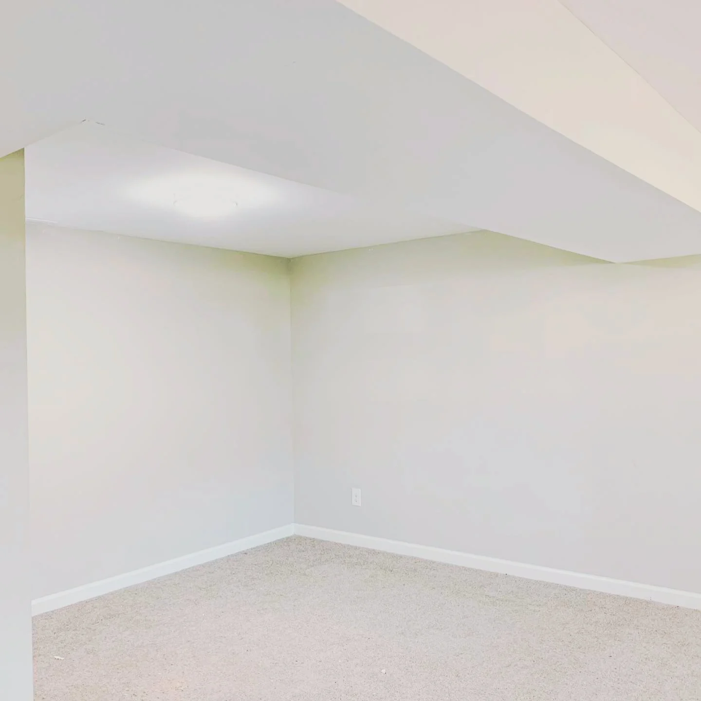 Empty room with white walls, beige carpet, and a sloped ceiling with a white light fixture.