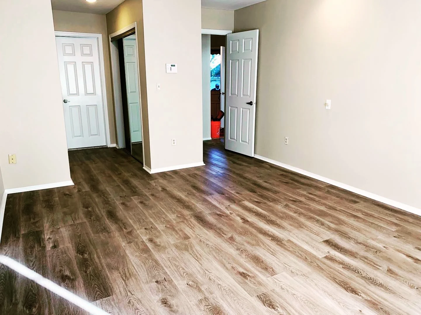Empty room with light beige walls, wooden flooring, a closet with sliding mirror doors, and an open door leading to an outside area.