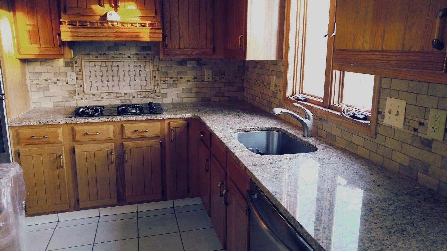 Kitchen with wooden cabinets, granite countertops, a brick backsplash, a double sink, a stove with two burners, and windows above the sink.